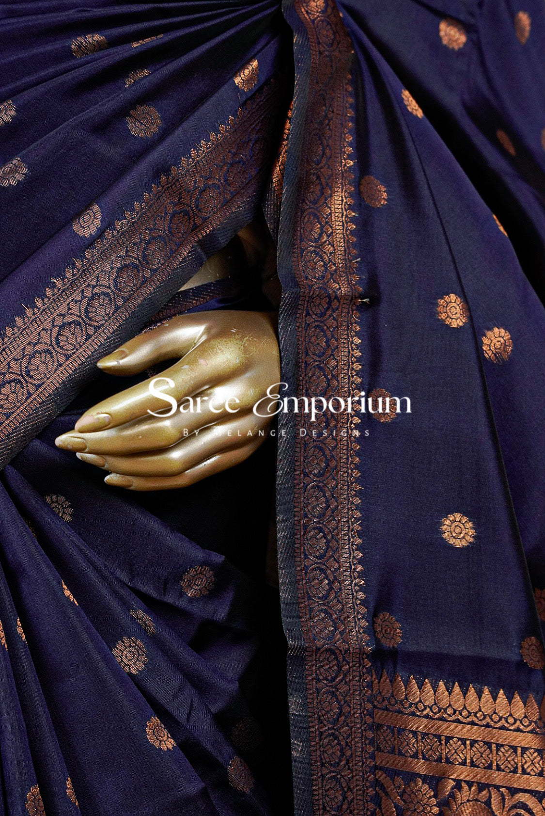 A close-up of a dark navy blue silk saree with intricate gold zari woven patterns and borders.