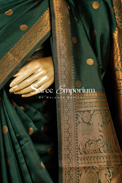 A close-up of a dark green silk saree with intricate gold zari woven patterns and a wide decorative border.