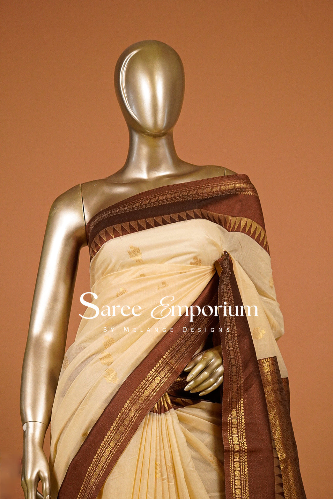 A cream-colored silk saree with coffe brown and gold borders draped .