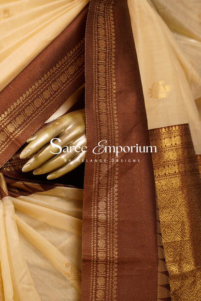 A close-up of a traditional Indian saree with a warm beige body, a rich coffe brown border, and intricate gold zari metallic embroidery.