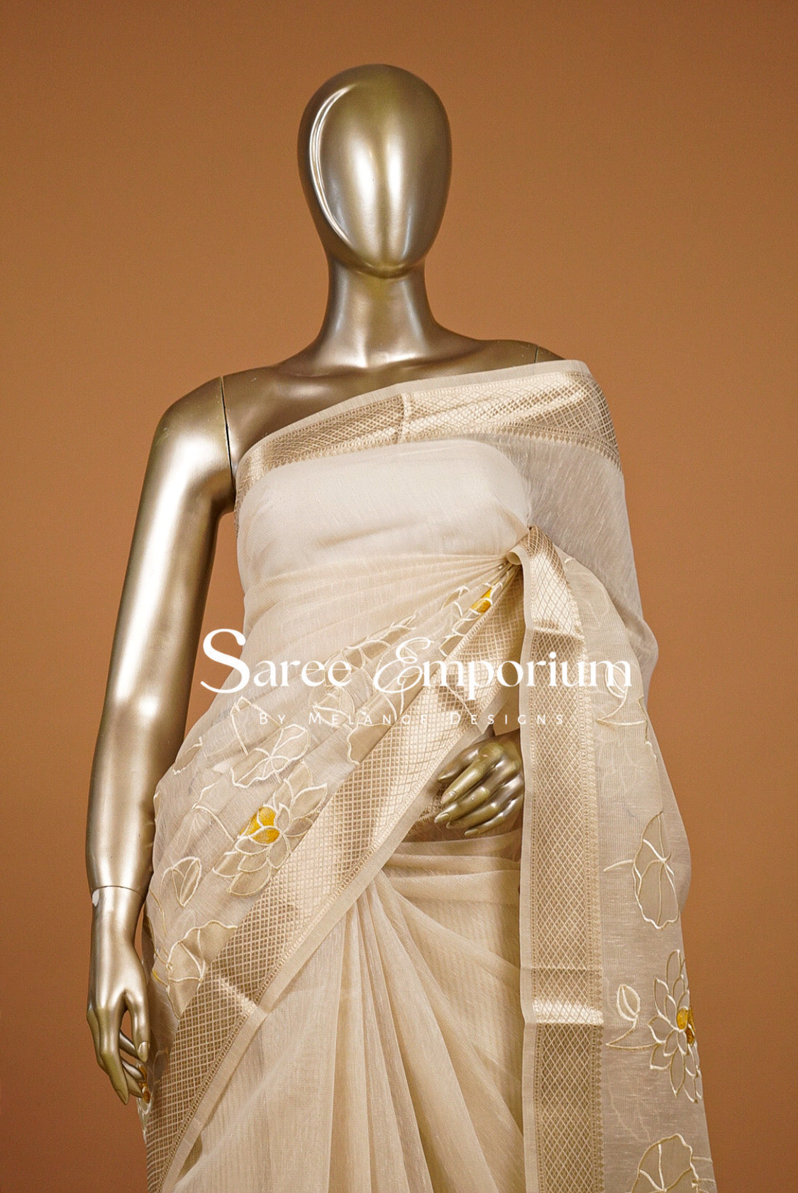 A cream-colored silk saree with gold floral embroidery.