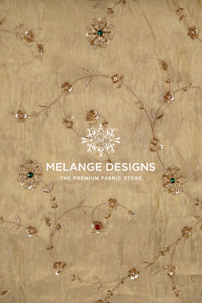 A close-up of a beige Tissue Silk Embroidery Fabric with delicate gold floral embroidery .
