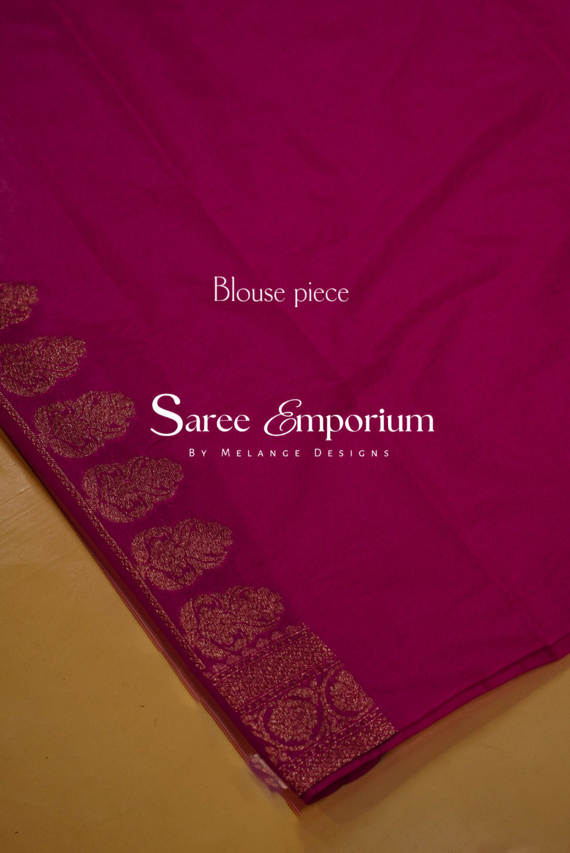 A close-up of a magenta pink saree blouse piece with a gold zari border pattern.