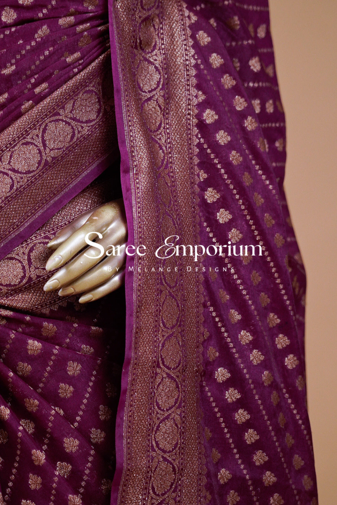 A close-up of a purple saree with metallic gold zari woven patterns and a wide border.