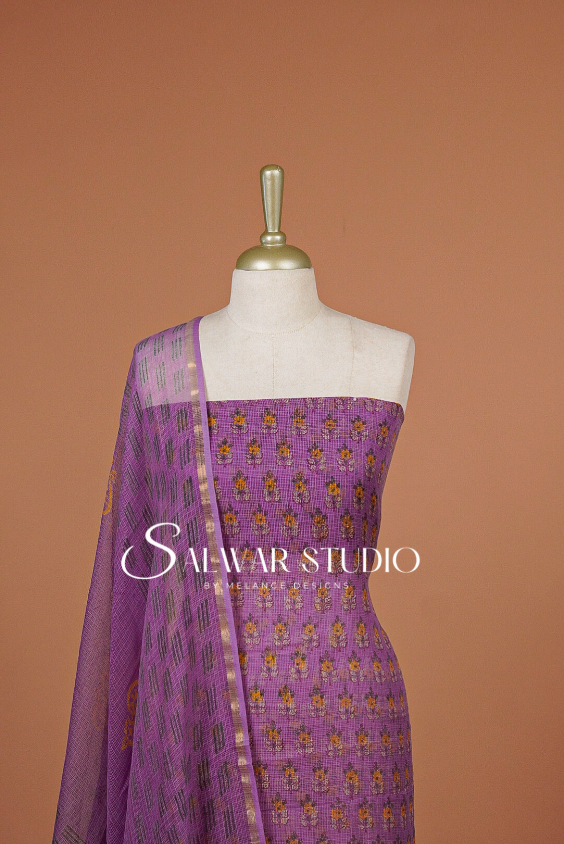 A lavender purple salwar suit set .The set includes a solid purple fabric top with small gold and yellow floral embroidery .