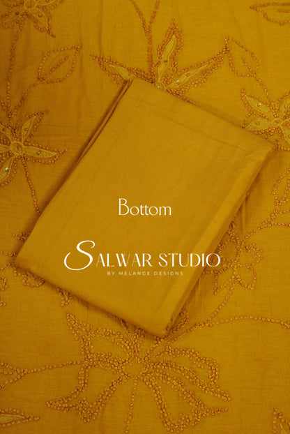 A folded mustard yellow fabric piece labeled 'Bottom' with placed on top of a matching embroidered fabric with floral and geometric stitching.