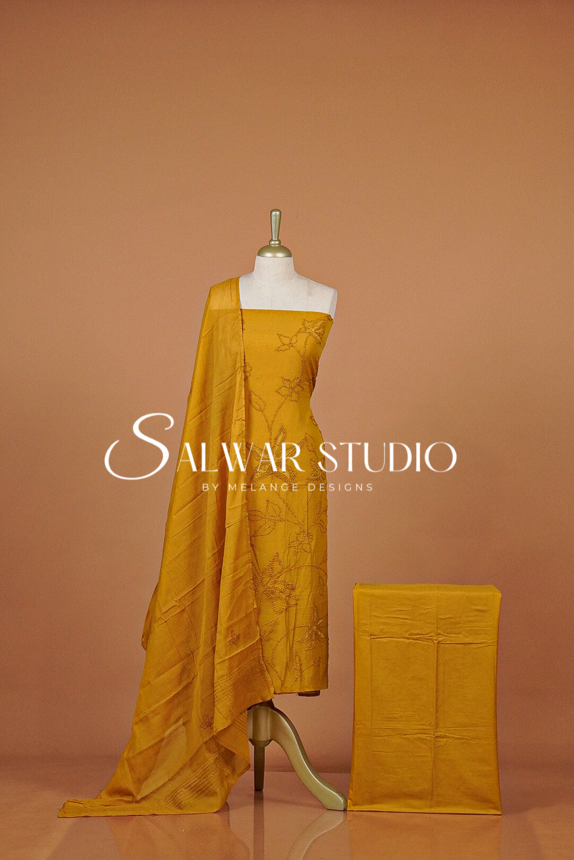 A mustard yellow salwar suit fabric set  with a matching folded fabric block beside it. 