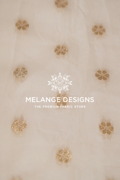 A close-up of a cream-colored Cotton Chanderi Brocade Dyeable  Fabric with scattered gold floral embroidery.
