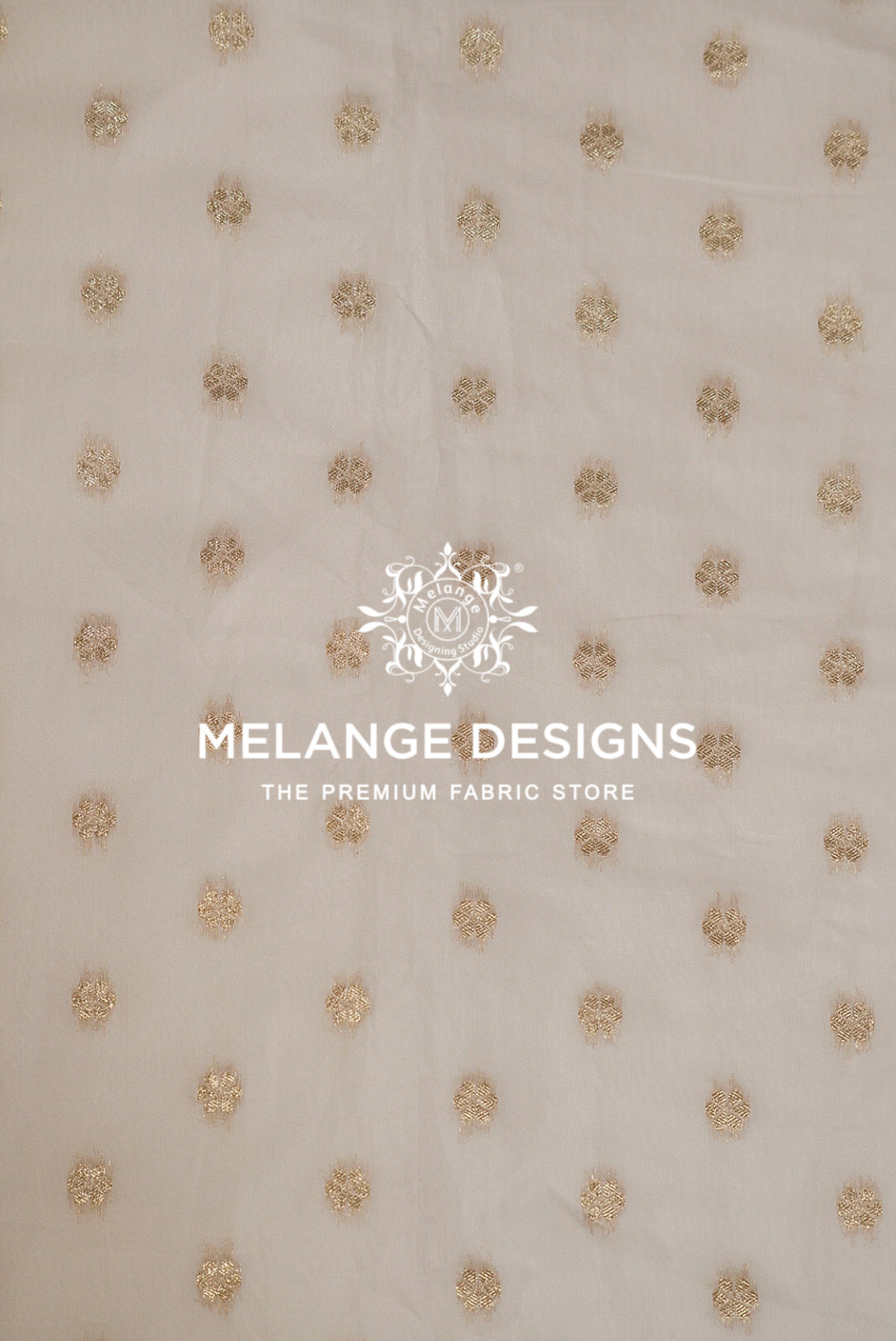 A close-up of a light beige Cotton Chanderi Brocade Dyeable  Fabric with a repeating pattern of small, textured gold floral or starburst motifs.