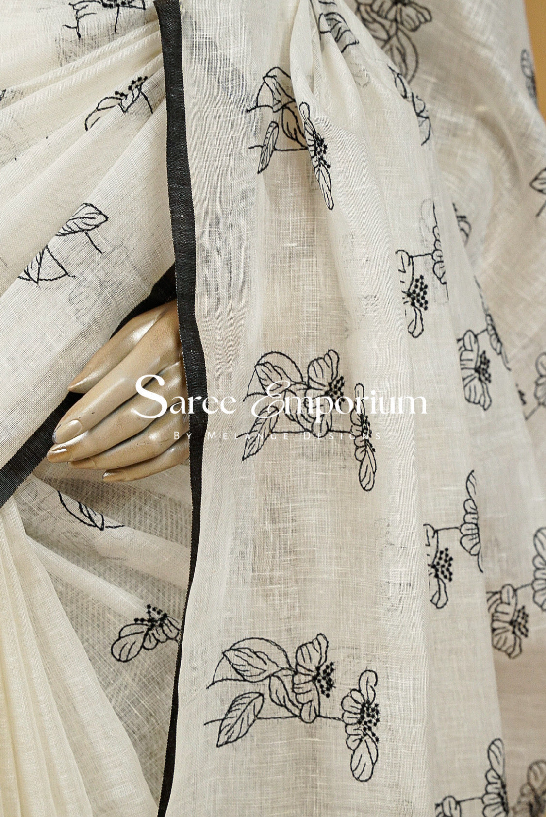 A close-up of a cream-colored saree with black floral line-art prints and a black border.