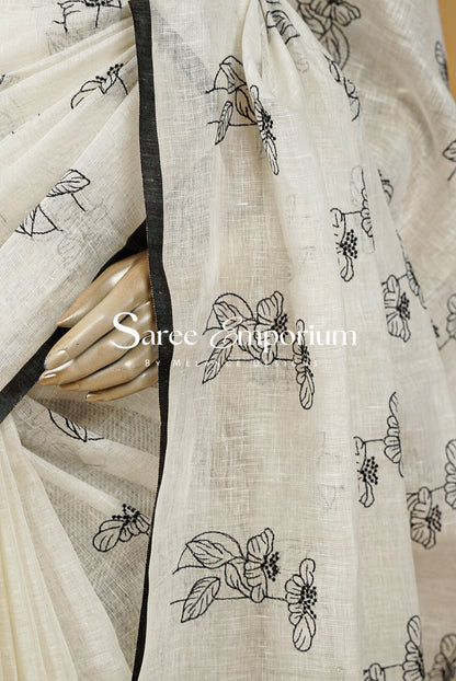 A close-up of a cream-colored saree with black floral line-art prints and a black border.