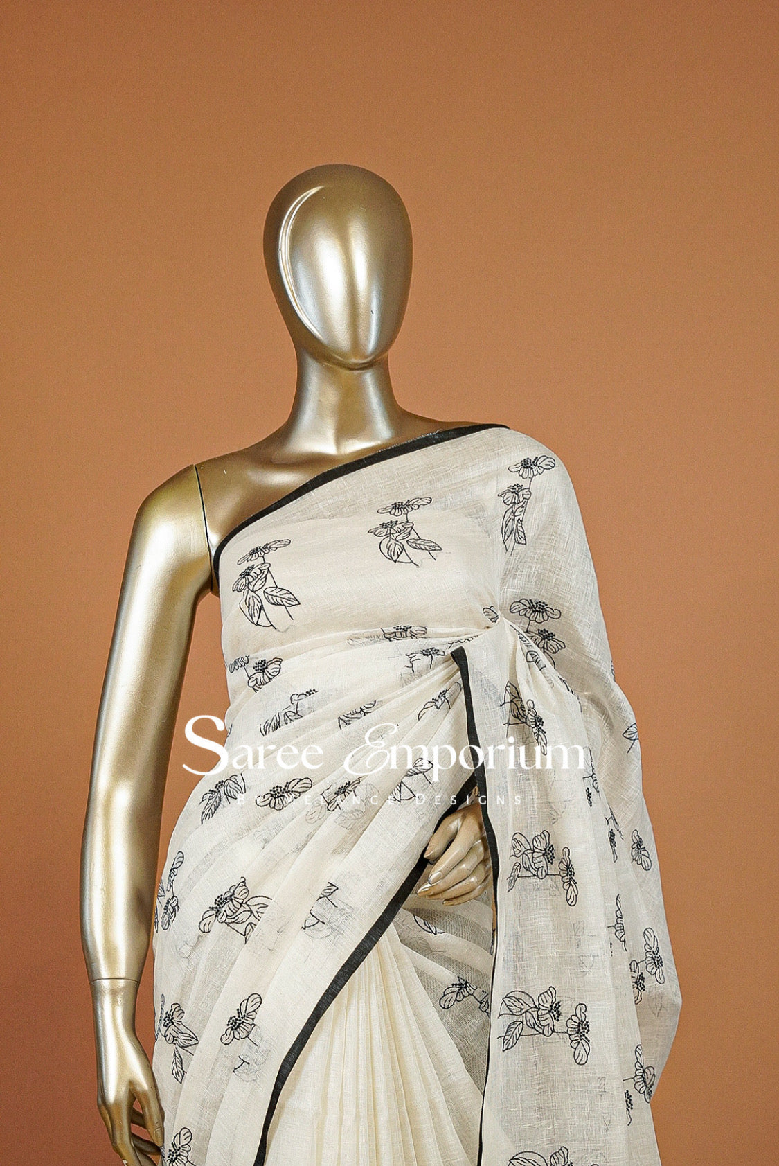 An off-white cotton saree with black floral prints and a black border.