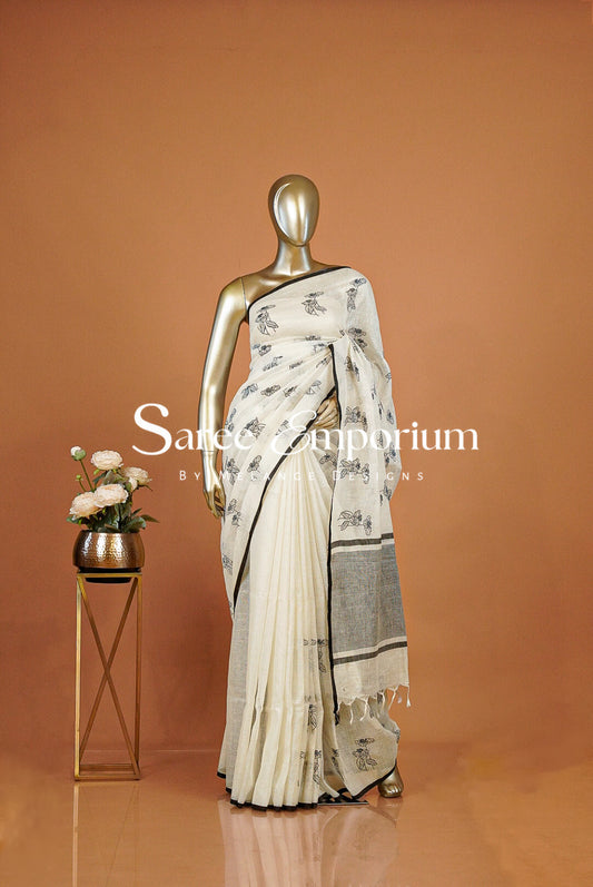 A cream and gray saree with black floral motifs .The saree features a pleated body and a draped pallu with a gray border.