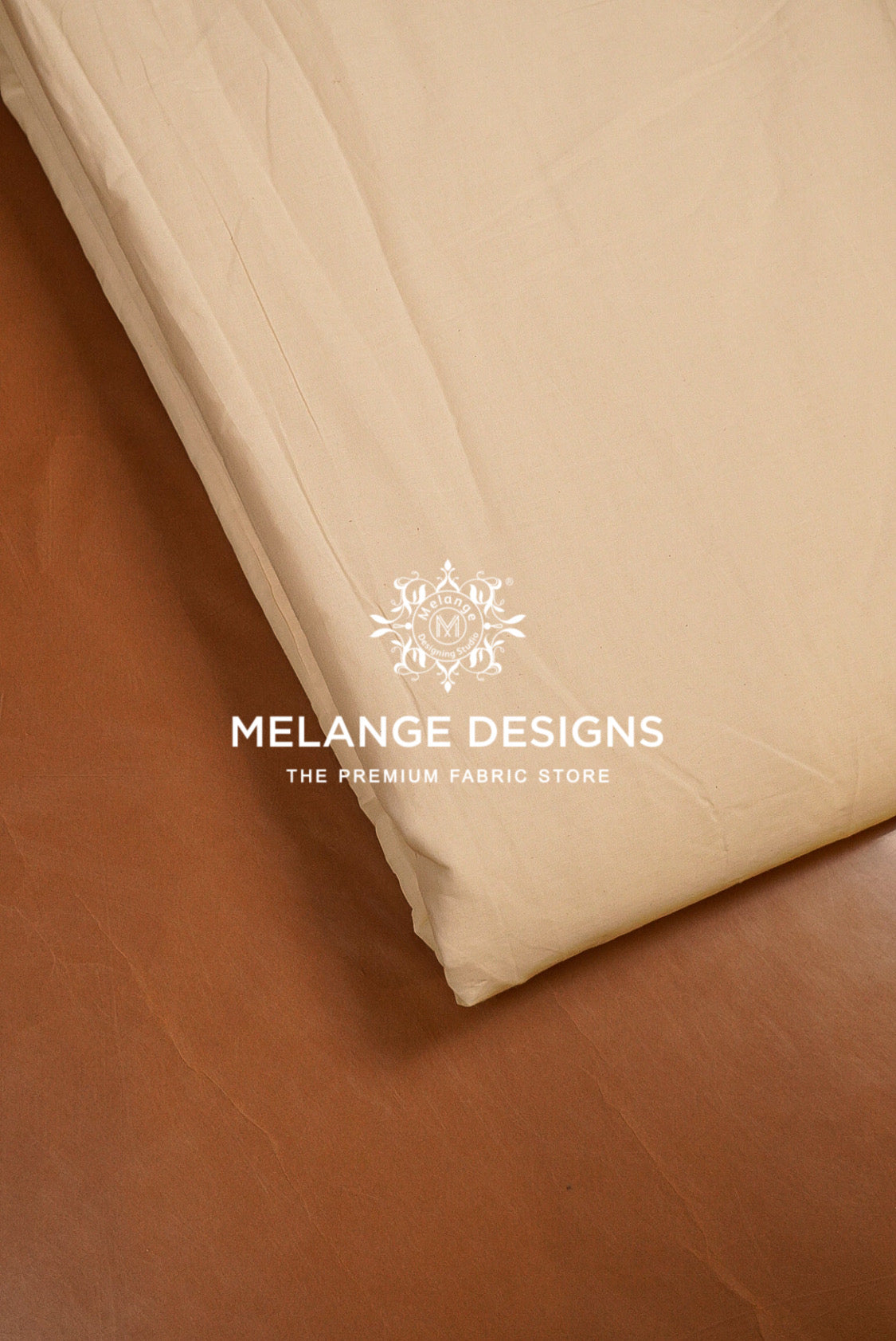 A close-up of a folded cream-colored Premium Cora Cotton Fabric Dyeable likely a bed sheet or duvet cover, resting on a brown leather surface. 