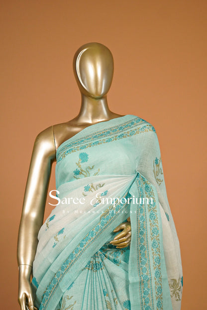 A light aqua blue and white saree with gold border and floral prints .