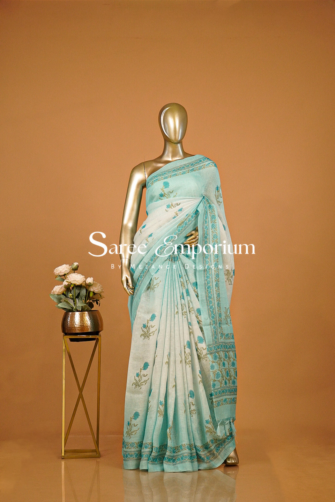 A light blue-green saree with gold and teal floral patterns.