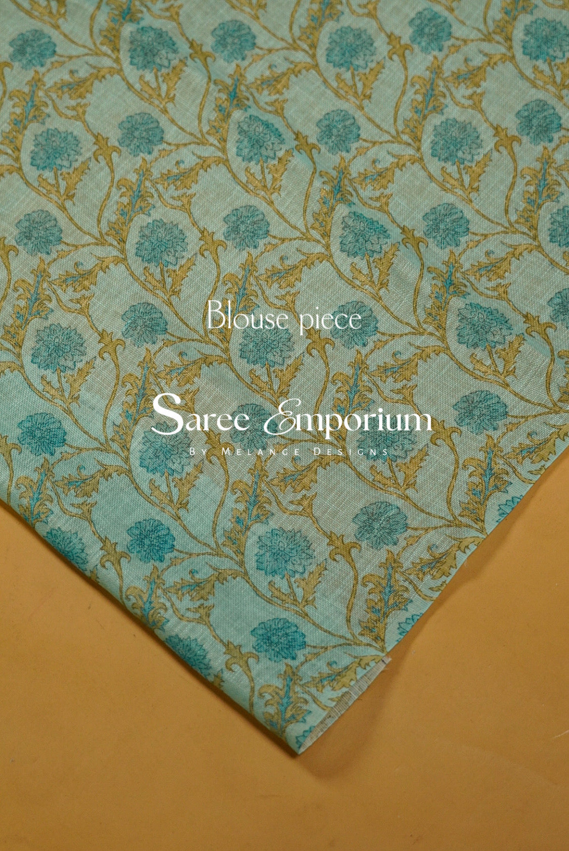 A folded piece of light blue-green sari fabric with a gold floral vine pattern.