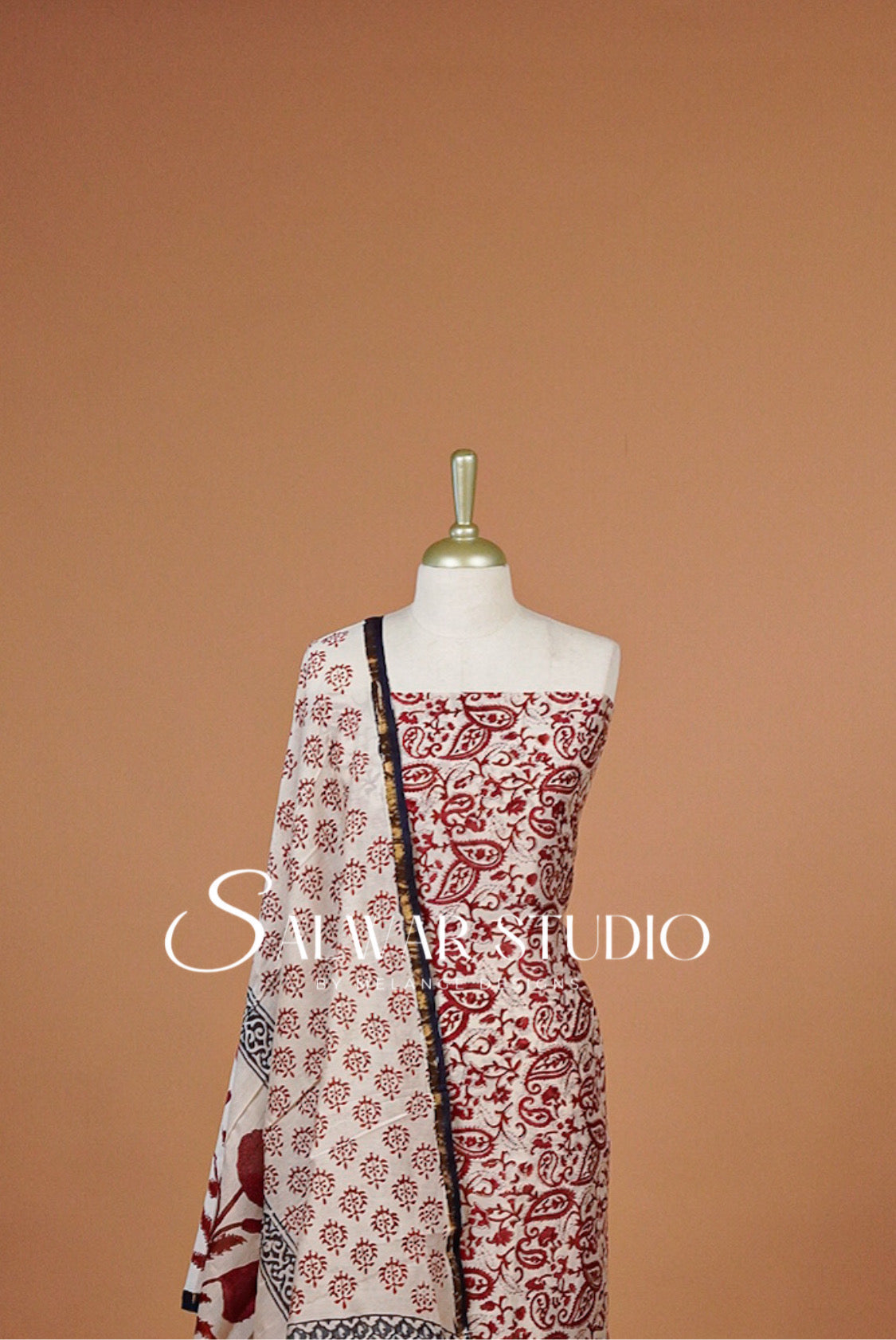 A sleeveless off-white dress with a red and black paisley print, styled with a matching patterned dupatta.
