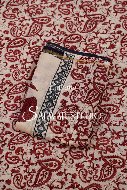 A folded piece of printed fabric or textile laid on top of a matching patterned fabric background. The folded item has a cream base with dark red paisley motifs, a dark blue border, and a small gold accent line near the top edge.