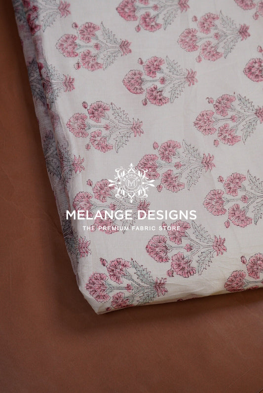 A folded piece of Printed Cotton Cotta Fabric  with a pink and gray floral block print on a white base, displayed on a brown surface. 
