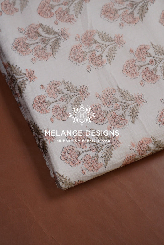 A folded piece of Printed Cotton Cotta Fabric with a floral pattern in dusty pink and muted green on a cream .