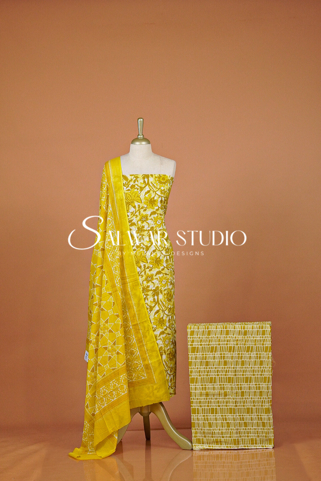 A yellow embroidered ethnic dress set with a matching woven fabric block beside it. 