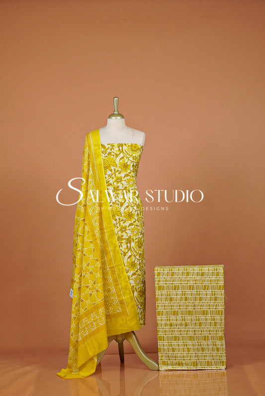 A yellow embroidered ethnic dress set with a matching woven fabric block beside it. 