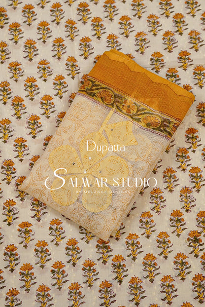 A folded dupatta fabric sample with a cream base and repeating orange and yellow floral block print, featuring a mustard yellow border and a decorative band with green and gold accents. 