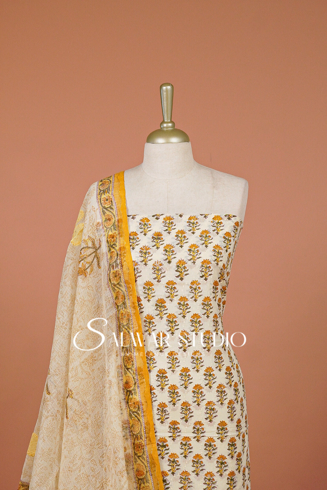 A cream-colored cotton fabric set with yellow and orange floral block prints,  with a matching printed dupatta against a solid terracotta.