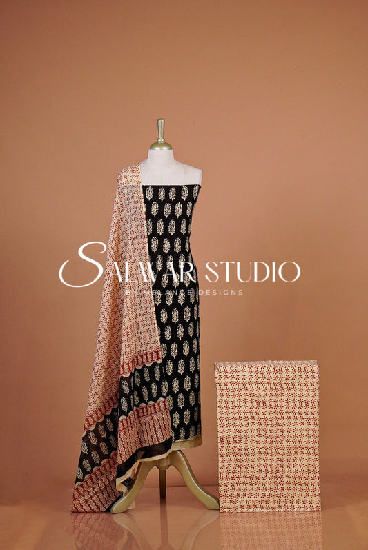 A women's salwar suit set displayed on a The set includes a black salwar with beige and white motifs, a beige printed dupatta with peach border details, and a matching beige printed fabric sample.