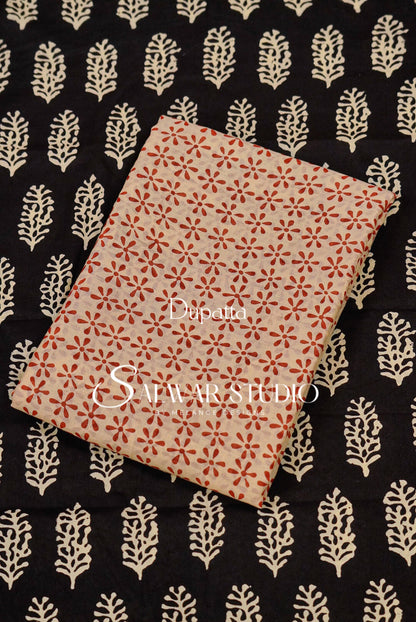 A folded piece of fabric with a red and beige block print pattern, displayed diagonally on top of a black fabric with a cream-colored leaf block print.