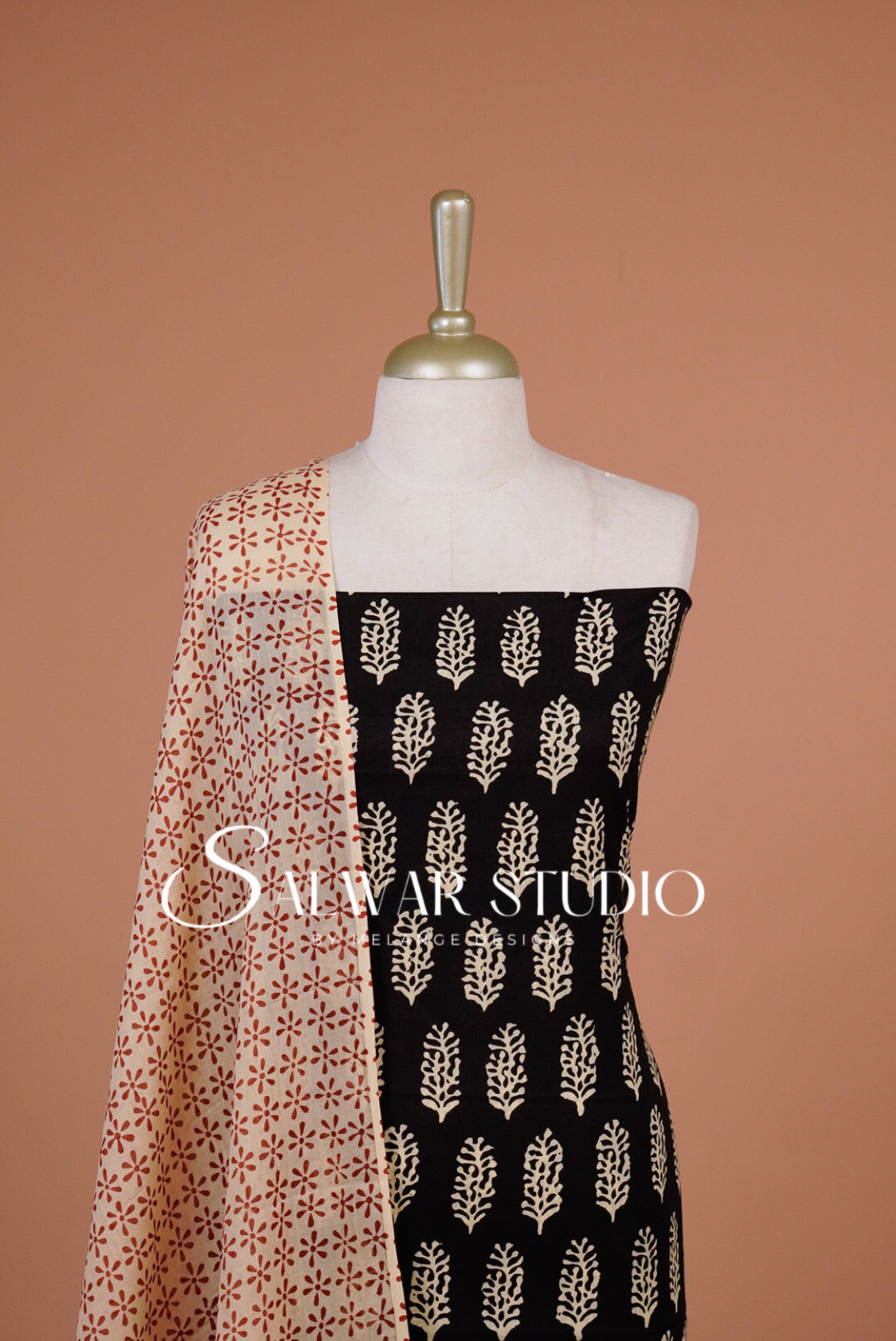 A mannequin torso displays a black fabric panel with beige leaf-like block prints and a peach dupatta.