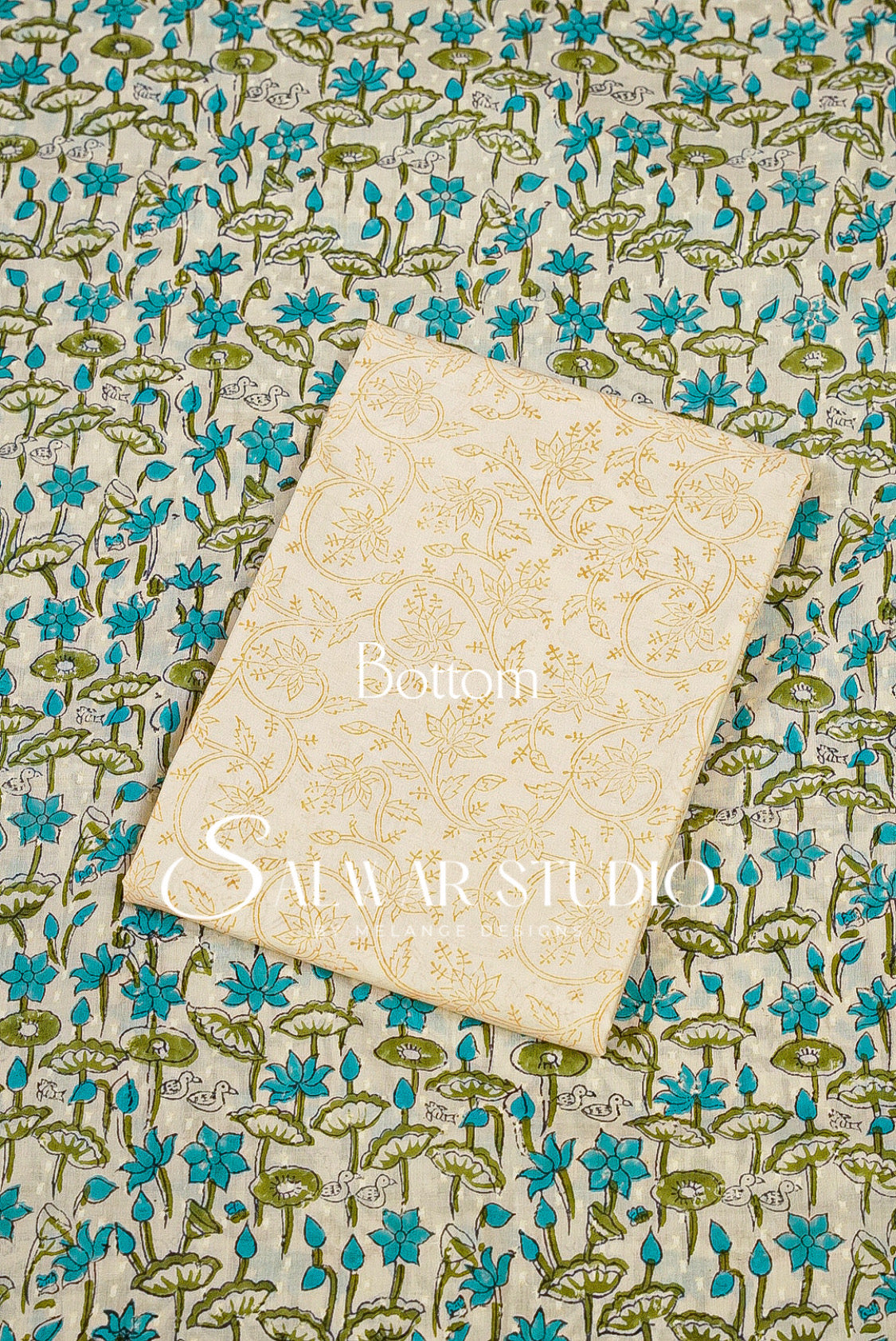 A cream-colored fabric bottom piece with a gold floral pattern, laid flat on top of a matching blue and green floral printed fabric. 