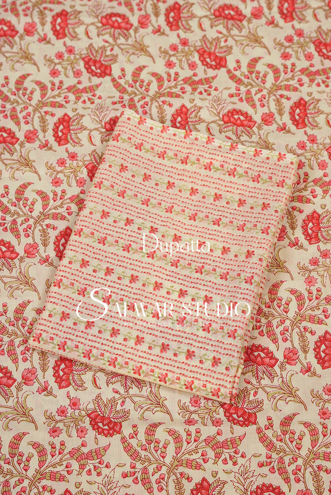 A folded piece of light pink and beige striped fabric with small floral motifs, placed on top of a larger cream-colored fabric with a red and gold floral pattern. 