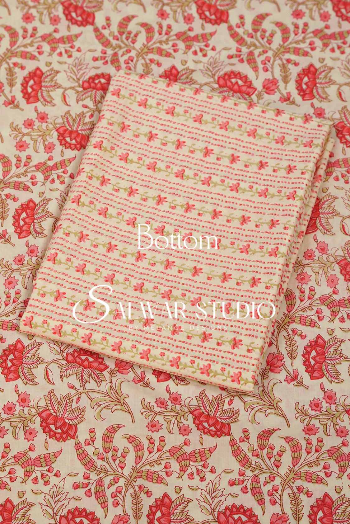 A folded piece of light pink and beige fabric with a delicate floral and geometric pattern, laid diagonally on top of a larger matching fabric sample featuring a red and gold floral print. 