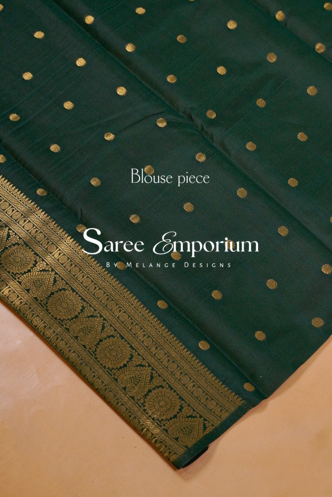 A dark green saree blouse piece with small gold polka dots and a wide gold patterned border.