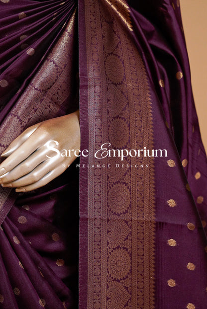 A close-up of a deep purple silk saree with metallic gold zari embroidery.