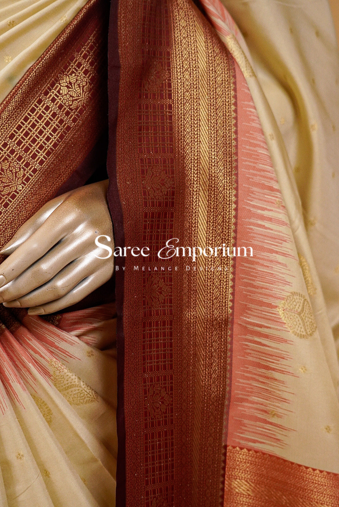 A graceful Semi Silk Saree in a soft ivory-cream tone, beautifully accented with a rich maroon and antique-gold zari border. Delicate golden woven motifs are scattered across the body, while subtle coral-red detailing along the border adds a refined traditional touch. The intricately woven pallu features elegant geometric and floral zari patterns for a luxurious finish.