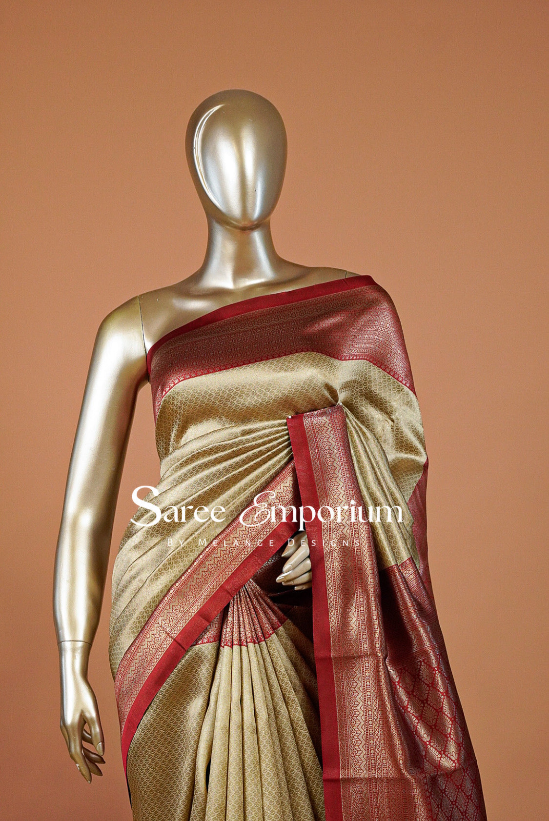 A gold-finished mannequin displays a beige and maroon silk saree with a metallic maroon border.