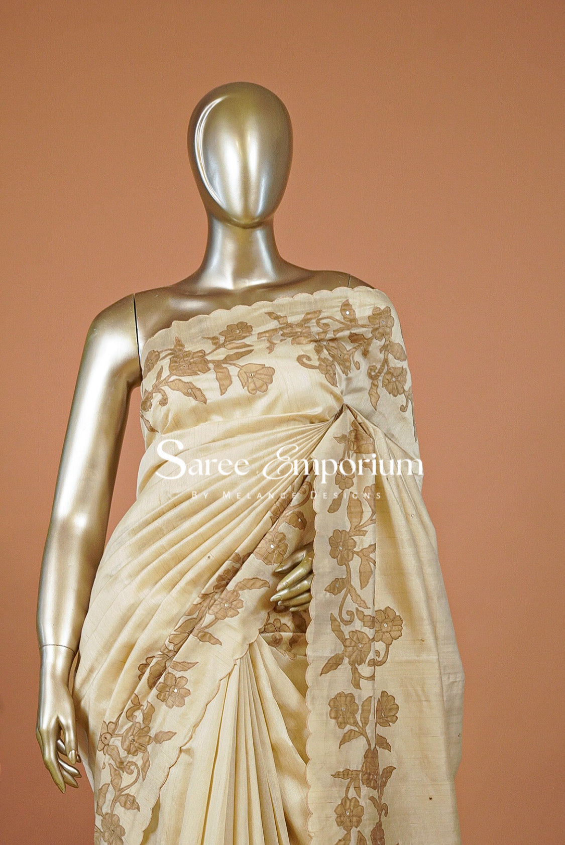 A cream-colored silk saree with gold floral embroidery draped .