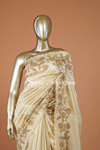 A cream-colored silk saree with gold floral embroidery draped .