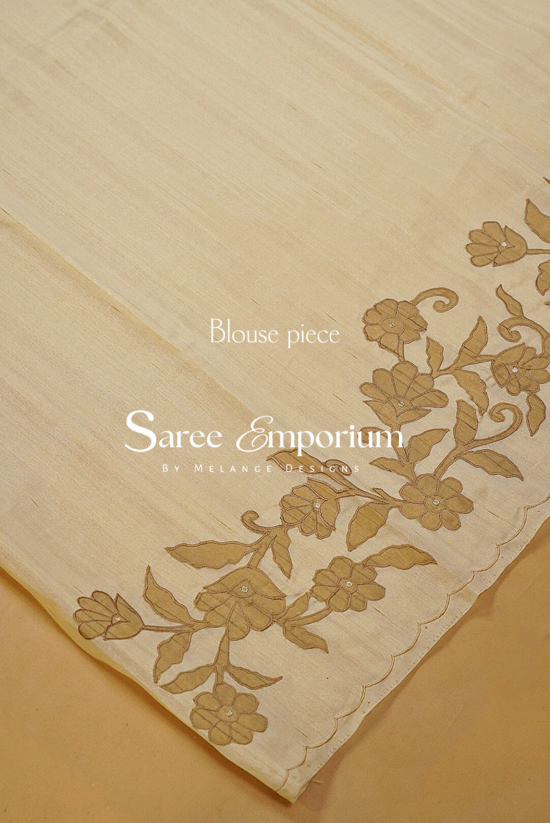 A close-up of a cream-colored fabric saree blouse piece with gold floral embroidery along the border.