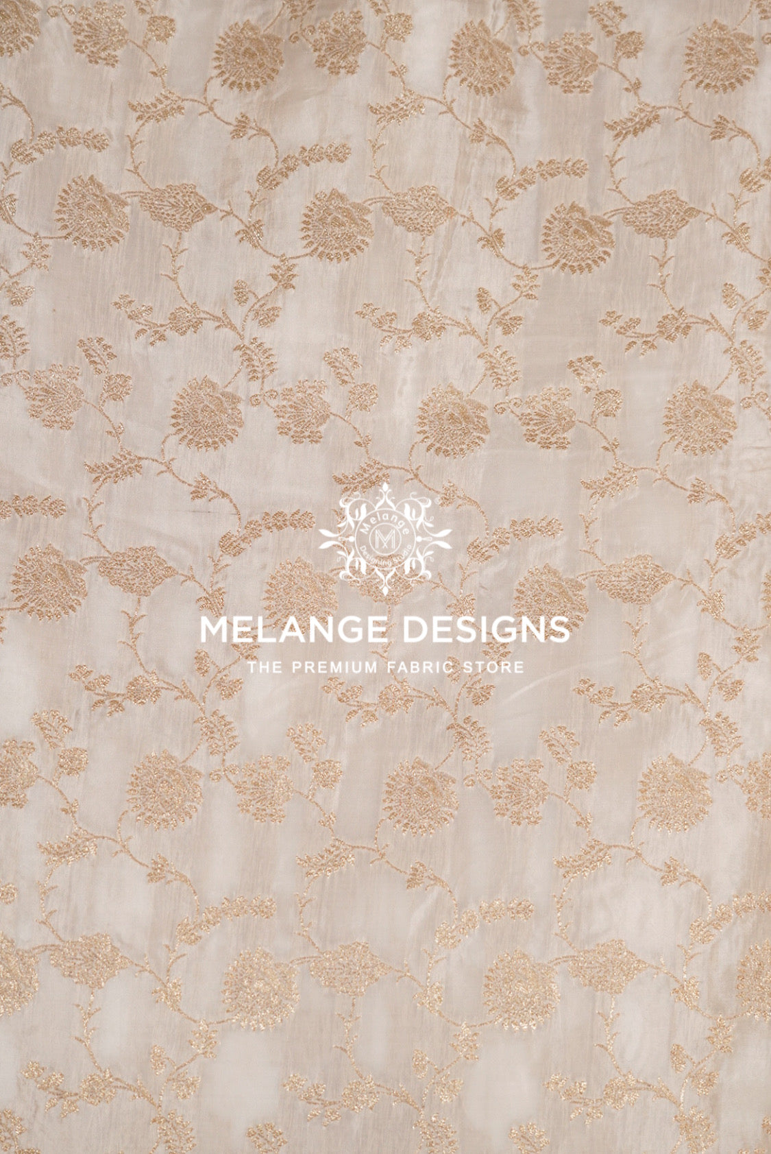 A close-up of a beige Silk Brocade Dyeable Fabric with an allover floral and vine pattern in a warm tan or light gold thread,