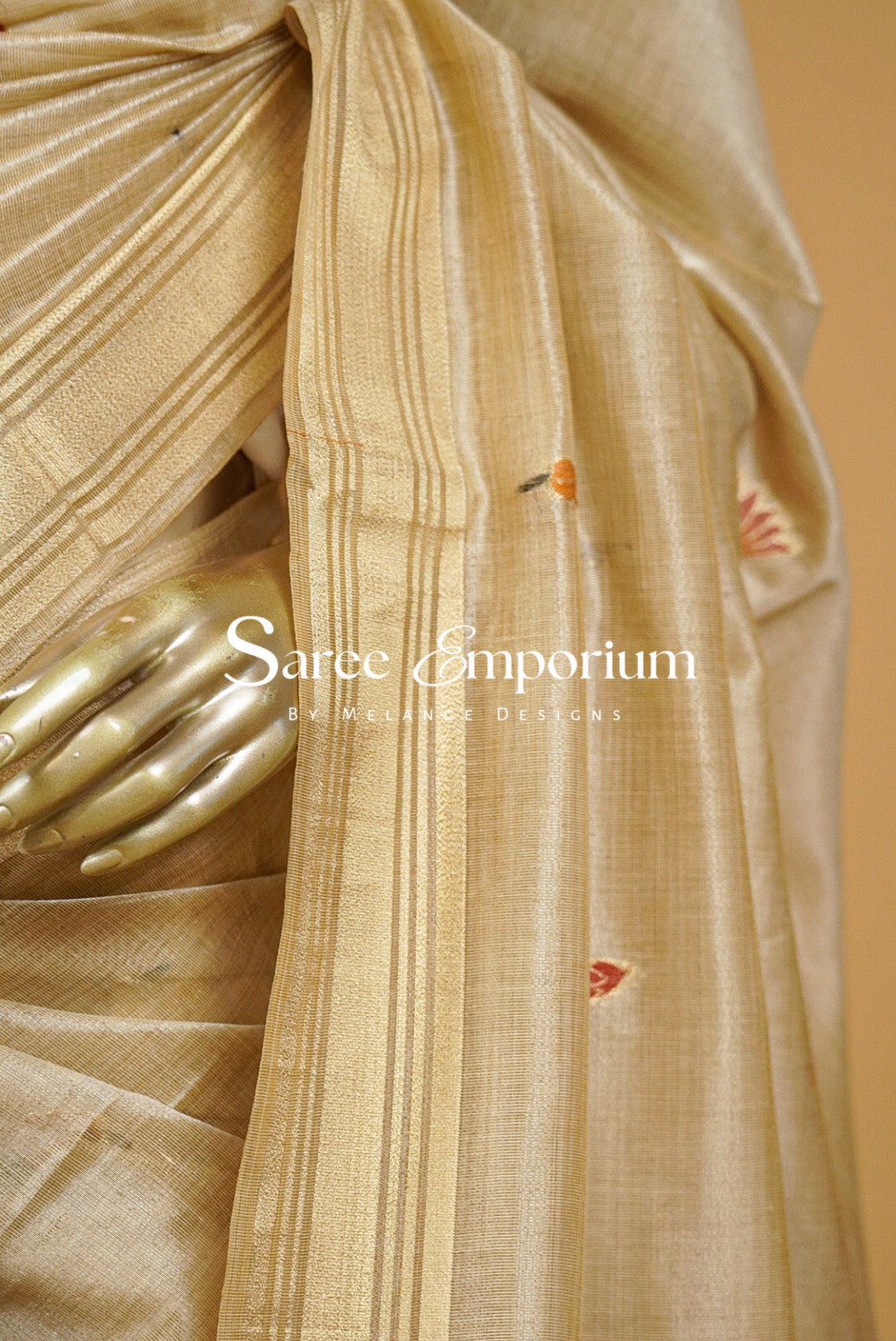 Champagne-Gold silk saree with vertical pleats and a border, featuring small red and orange embroidered motifs. 