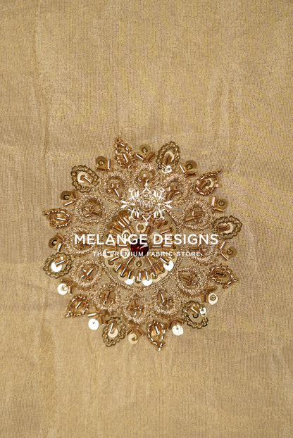 A circular, ornate gold sequin and bead embellishment with metallic gold embroidery, displayed on a textured beige Tissue Silk Embroidery Fabric .